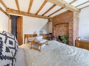 A cozy bedroom with a bed, a wooden bench, a brick fireplace, and a fluffy white rug. - 4 bedroom accommodation in Welshpool (Welshpool)