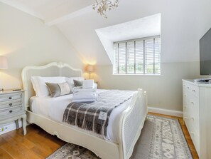 A bedroom with a white bed, bedside lamps, a small window, and a TV on a dresser. - 4 bedroom accommodation in Welshpool (Welshpool)