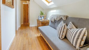Een knus interieur met een houten vloer, een grijze bank met gestreepte kussens, een houten nachtkastje met een plant en een spiegel aan de muur.
