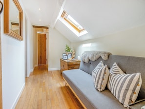A cozy room with a wooden floor, a grey sofa with striped pillows, a wooden nightstand with a plant, and a mirror on the wall. - 4 bedroom accommodation in Welshpool (Welshpool)