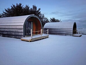 Two snow-covered arched structures with wooden decks and rope barriers, surrounded by trees.