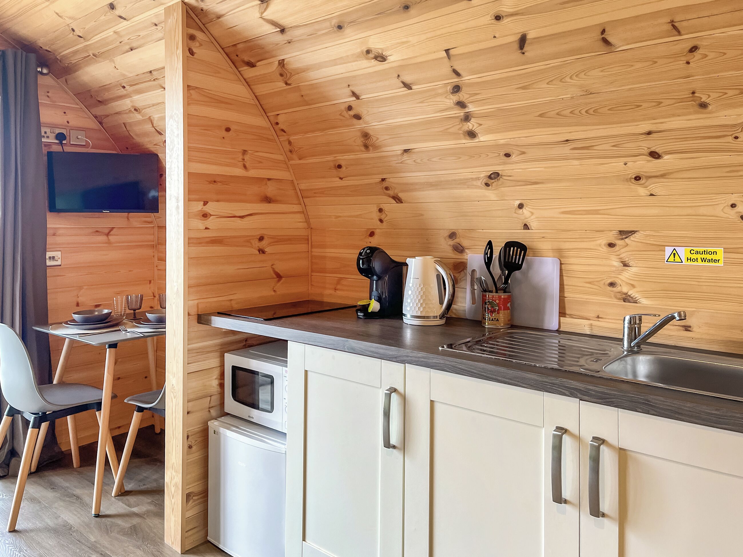 A compact kitchen with wooden walls, a microwave, a kettle, and a sink.