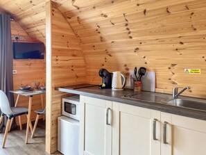 A compact kitchen with wooden walls, a microwave, a kettle, and a sink.