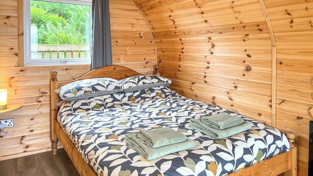 A wooden cabin room with a bed, a window with curtains, and a view of greenery outside. - 1 bedroom accommodation in Stranraer (Stranraer)