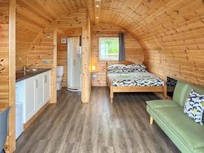 Ein gemütliches, hölzernes Interieur mit einem Bett, einem grünen Sofa, einem Badezimmer und einer Küchenzeile.