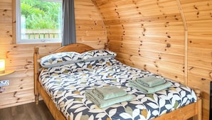 A cozy wooden room with a bed, a window with curtains, and a bedside table with a lamp.