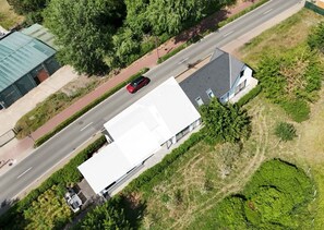 Eine Vogelperspektive eines Gebäudes mit flachem Dach, neben einer Straße mit einem roten Auto, umgeben von Grünflächen und einem gepflasterten Gehweg.