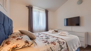 Un dormitorio con cama, televisión y ventana con cortinas.