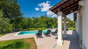 Una piscina con sillas de descanso, rodeada de follaje y una estructura de pérgola.