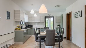 Una cocina moderna con comedor, que cuenta con una isla central, iluminación colgante y vistas al exterior.