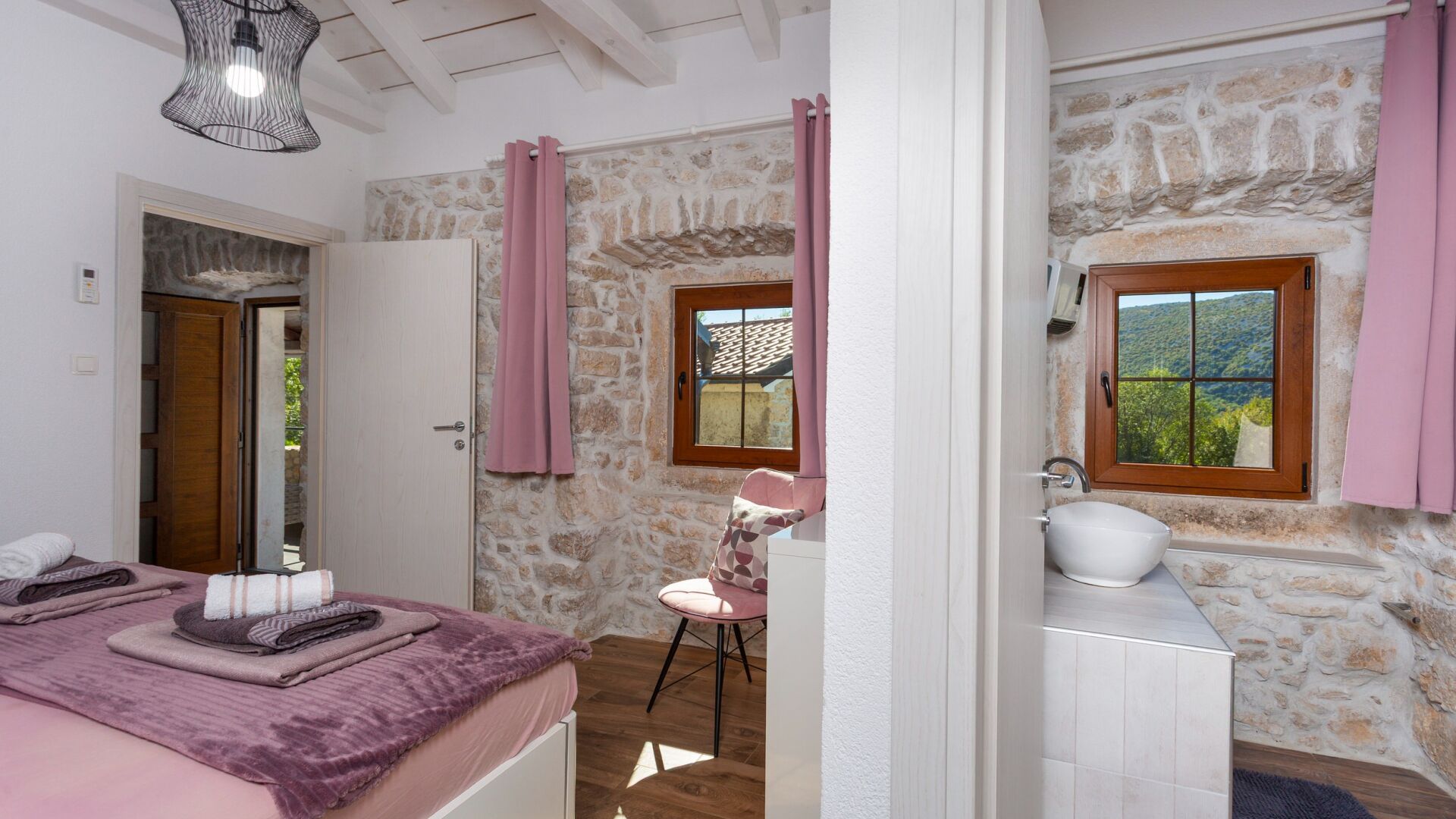 A bedroom with a bed, a chair, a bathroom with a sink, and a stone wall.