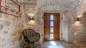 A stone-walled corridor with a wooden door, a wicker chair, and a wall-mounted light fixture. - Villa Mariva residence Crikvenica by Villas Guide (Tribalj)
