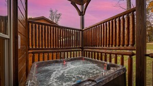 A hot tub on a wooden deck with a wooden railing, surrounded by trees.