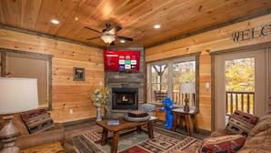 A wooden interior with a fireplace, a TV mounted on the wall, and a welcome sign.
