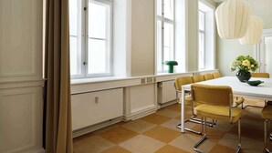 A dining area with a white table, yellow chairs, and a green chair. There are large windows with white frames and a checkered floor.