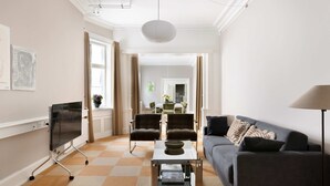 A living room with a sofa, two armchairs, a coffee table, and a flat-screen TV on a stand.
