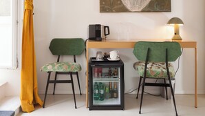 Una habitación compacta con dos sillas, un refrigerador pequeño con bebidas, una cafetera y una mesa con lámpara.
