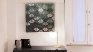 Un escritorio con cafetera, una lámpara y una silla en una habitación con radiador y ventana.