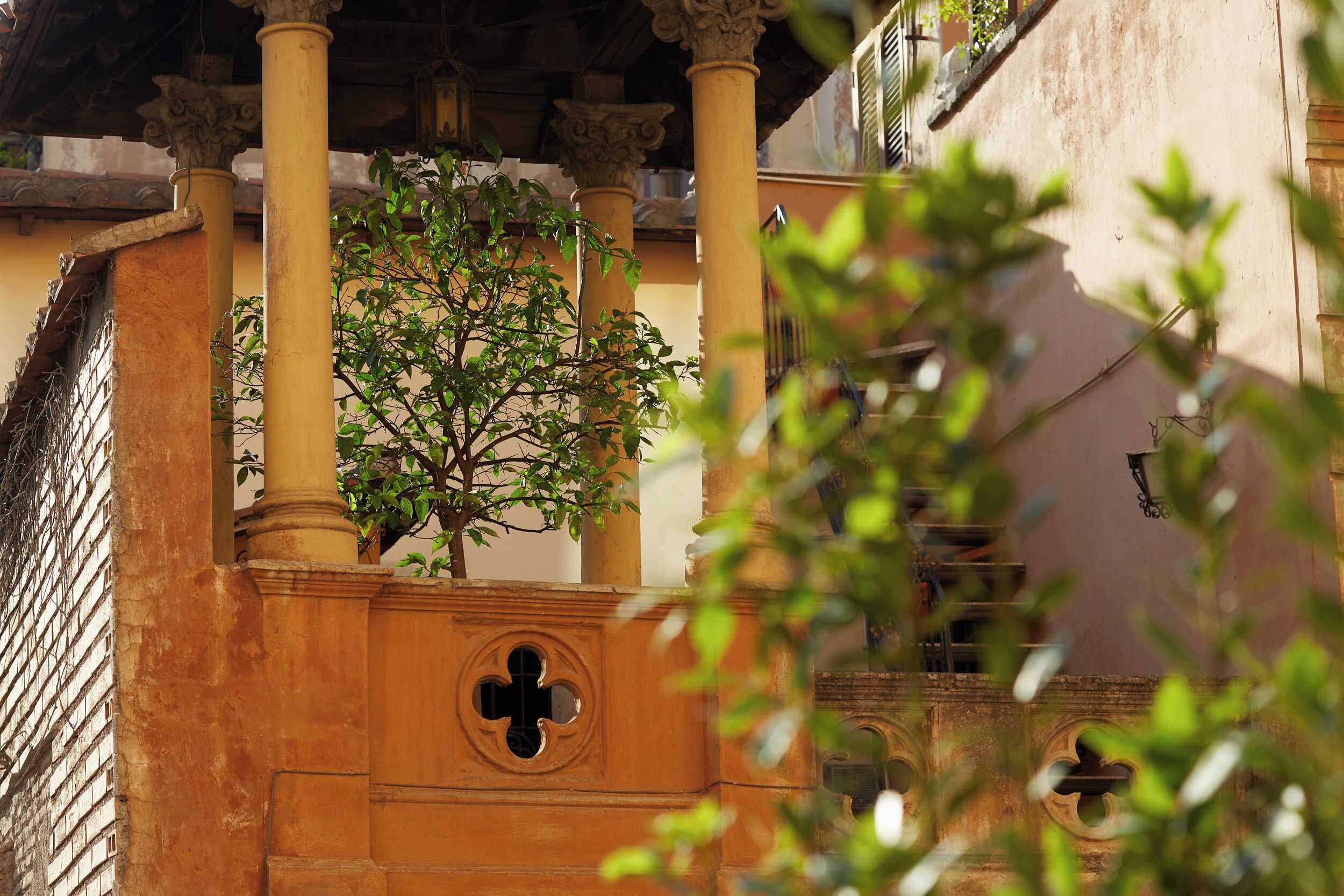 Un edificio con balcón, columnas y un árbol.