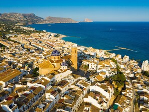 Vista aérea de un pueblo costero con edificios blancos, una iglesia destacada con cúpula y un mar azul cristalino.