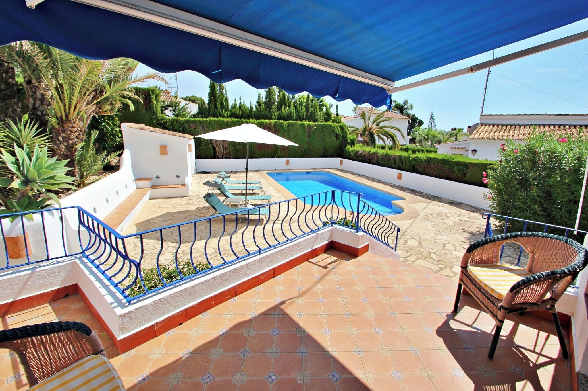 An outdoor pool area with a blue canopy, lounge chairs, and a small white structure.