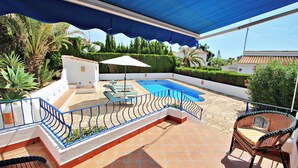 An outdoor pool area with a blue canopy, lounge chairs, and a small white structure.