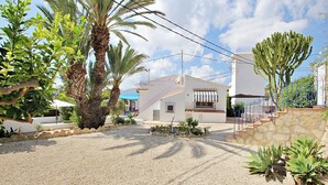 A white building with a staircase leading to a balcony, surrounded by palm trees and cacti.