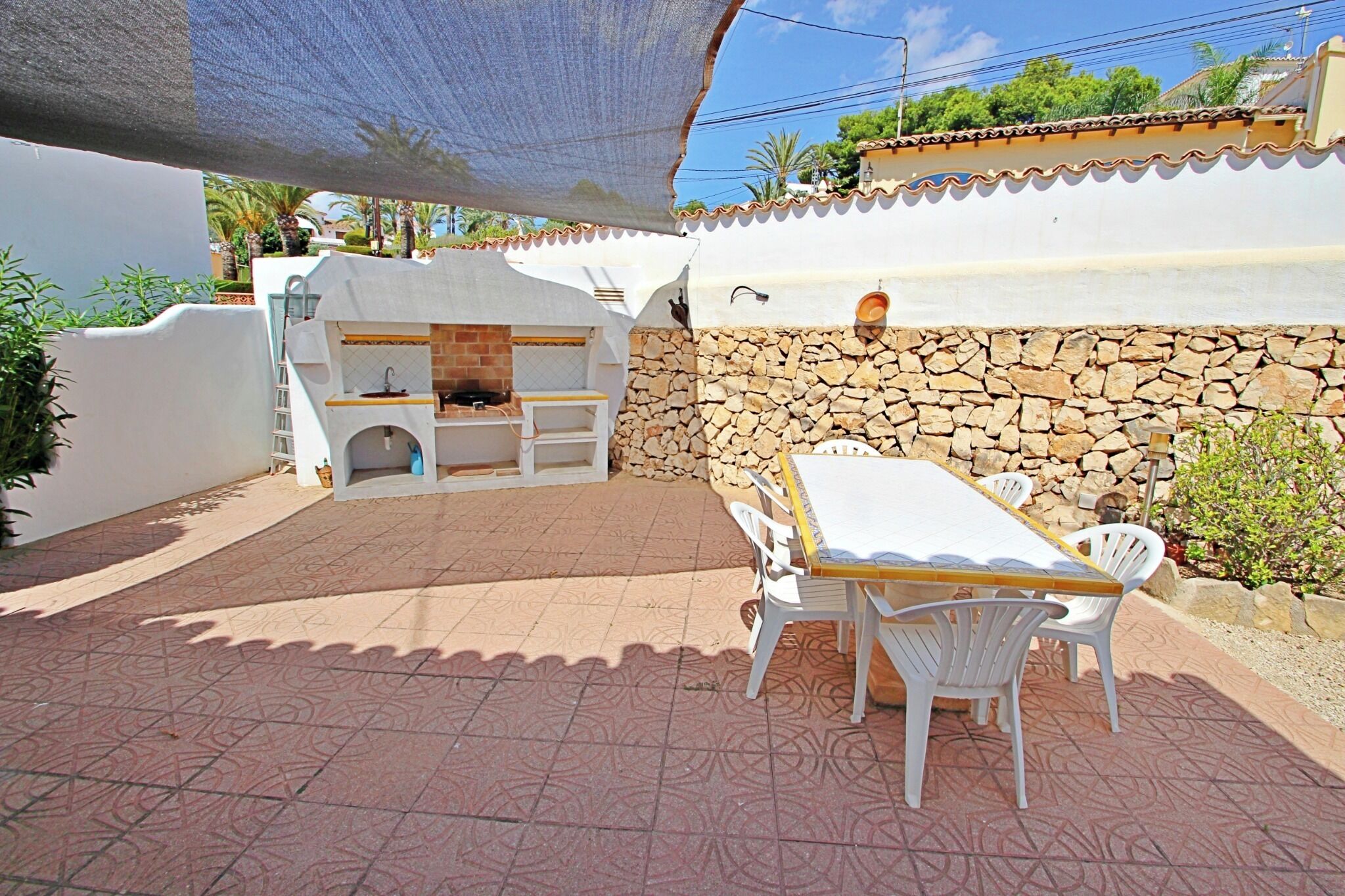 Un patio exterior con pared de piedra, zona de barbacoa y mesa con sillas.