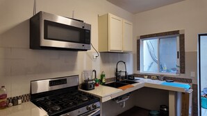 A compact kitchen with a microwave, stove, and sink. There is a window with a view of the outside.