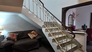 A staircase with a marble finish and metal railings, leading to a second floor. A dark-colored sofa with patterned cushions is positioned in the foreground.