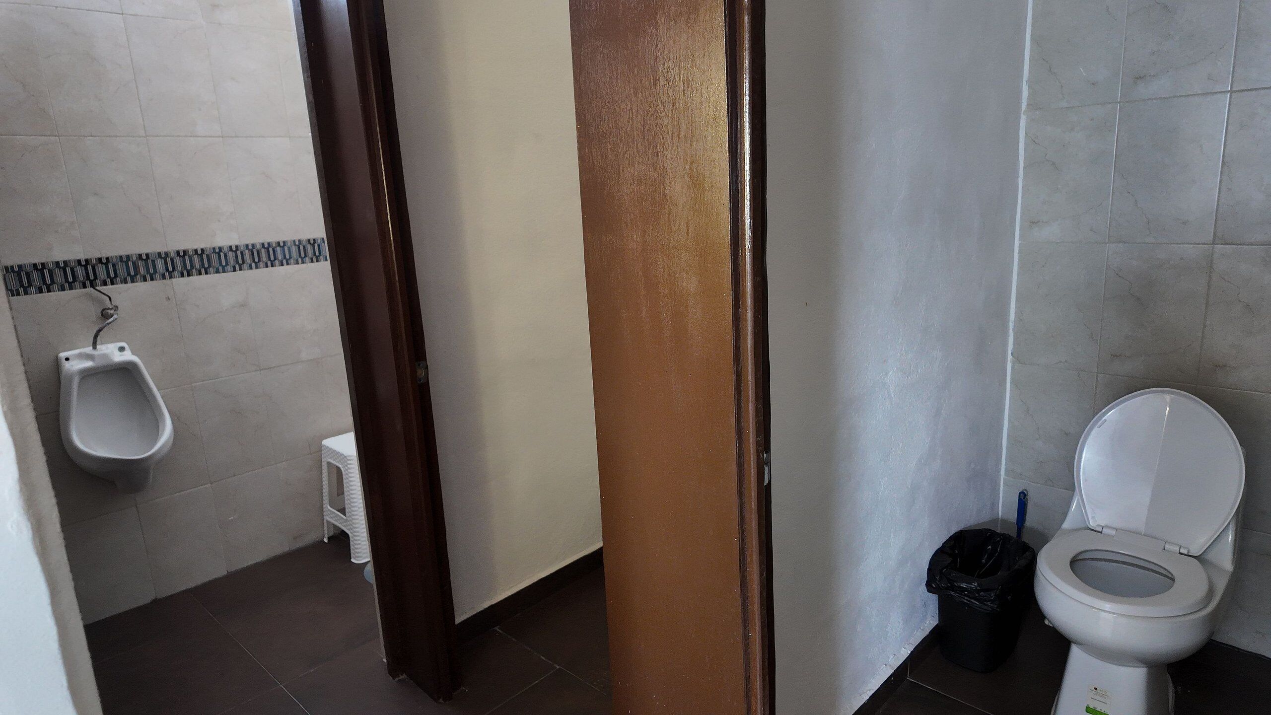 A bathroom with a urinal, toilet, and a trash bin.