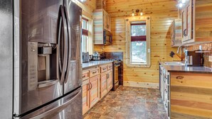 A modern kitchen with stainless steel appliances, wooden cabinets, and a stone tile floor. - Steps to Marina & Beach: Couple’s Cottage in Pepin (Pepin)
