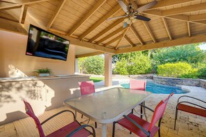 Eine Außenpatio mit Tisch, Stühlen, einem Deckenventilator und einem an der Wand befestigten Fernseher.
