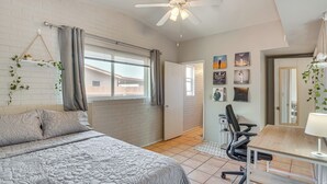 Un dormitorio con cama, escritorio, silla, ventilador de techo y ventana con cortinas.