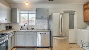 Una cocina con armarios blancos, lavavajillas, refrigerador y lavadora.