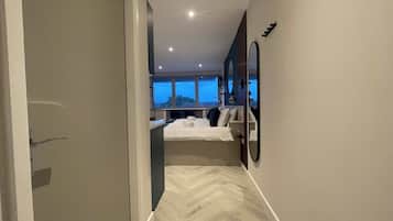 Een moderne hotelkamer met een groot bed, een zithoek met een fauteuil en uitzicht op het landschap door een raam.