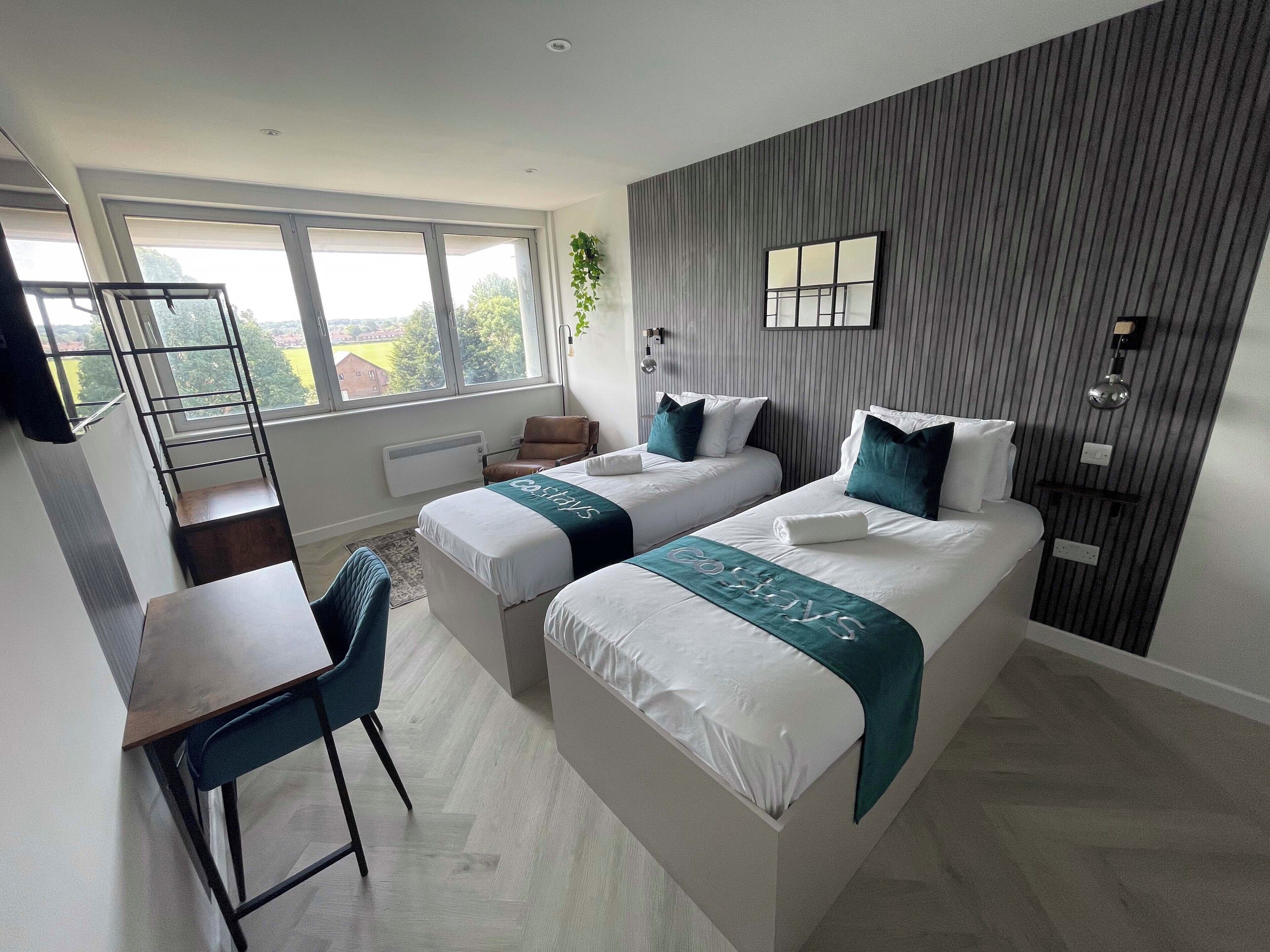 A modern hotel room with two beds, a desk, and a chair.