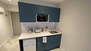 A compact kitchen with dark blue cabinets, a white countertop, a microwave, a toaster, a kettle, and a sink.
