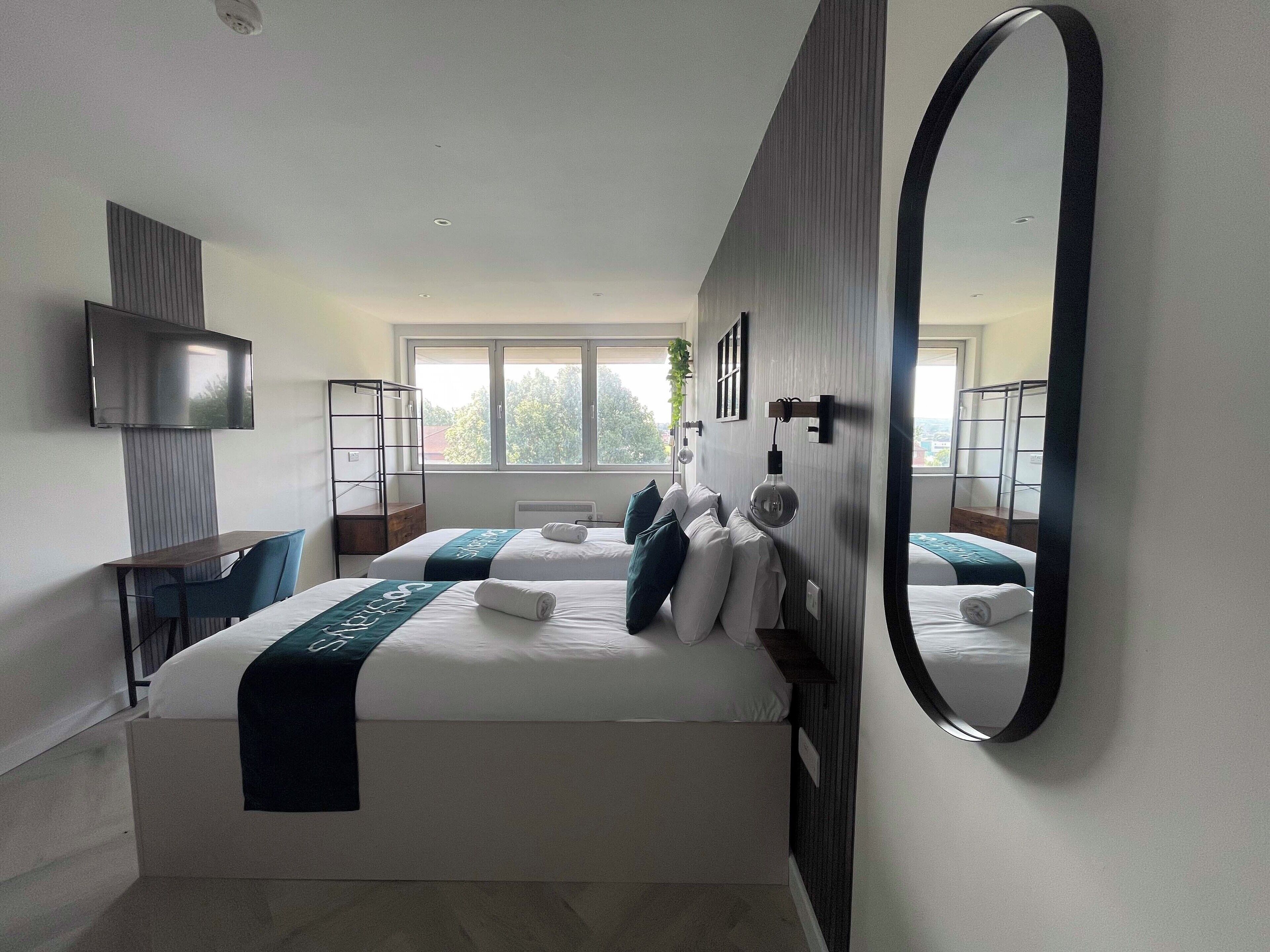 Une chambre d’hôtel moderne équipée de deux lits, d’un bureau, d’une télévision et d’un grand miroir.