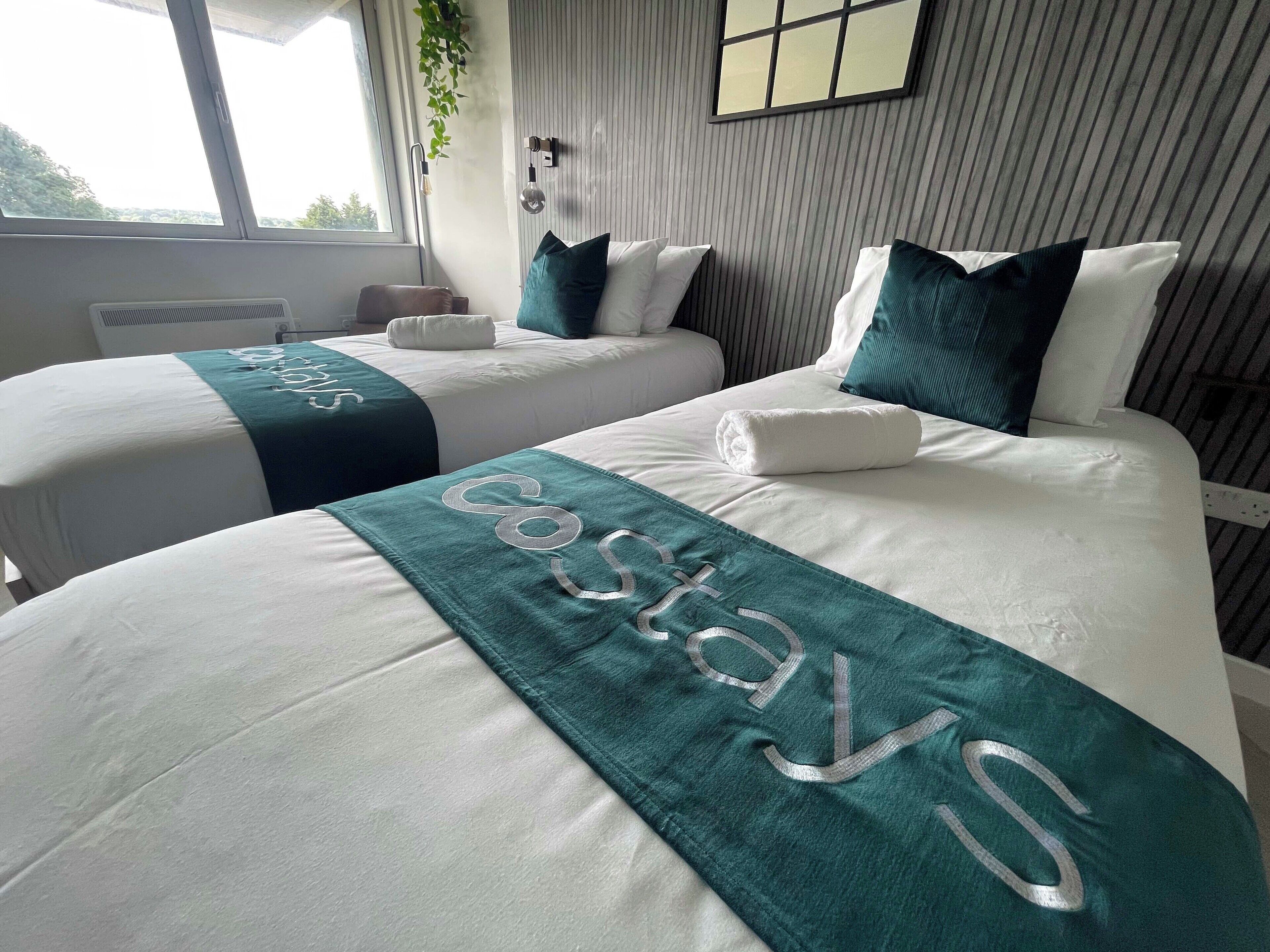 A hotel room with two beds, each with a teal bedspread and a towel.