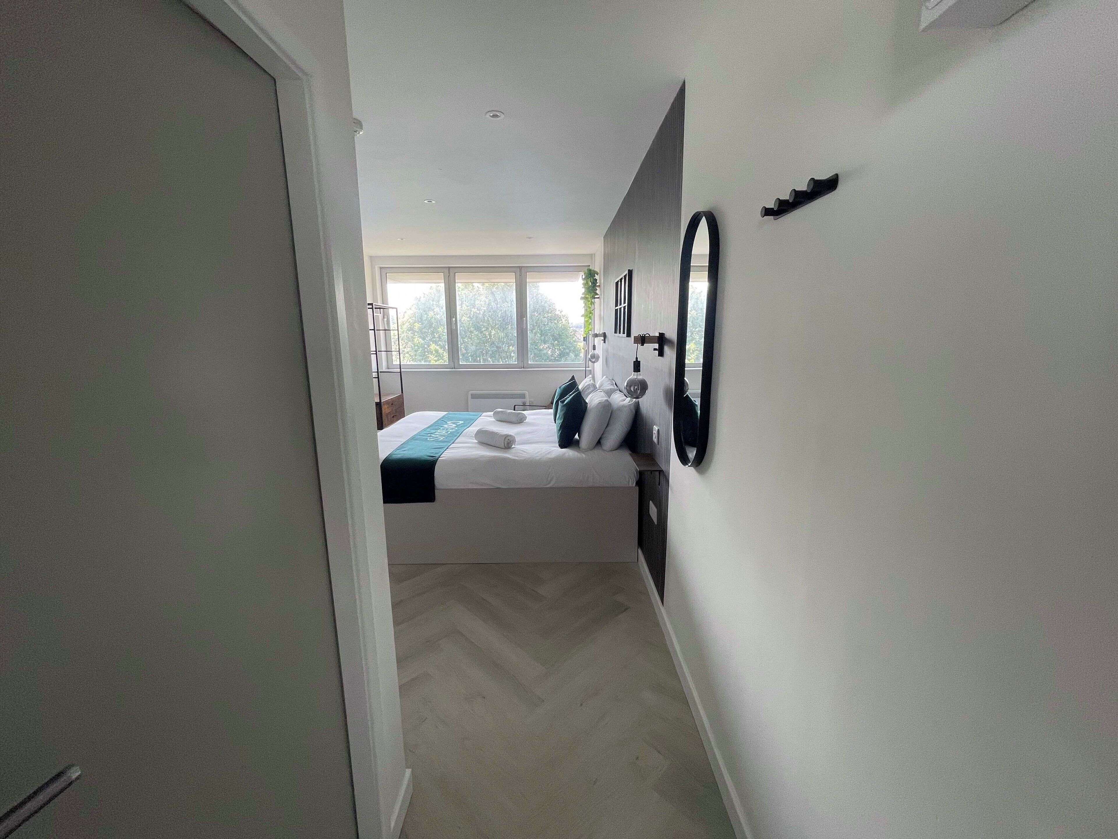 A modern bedroom with a bed, bedside tables, a mirror, and a window.