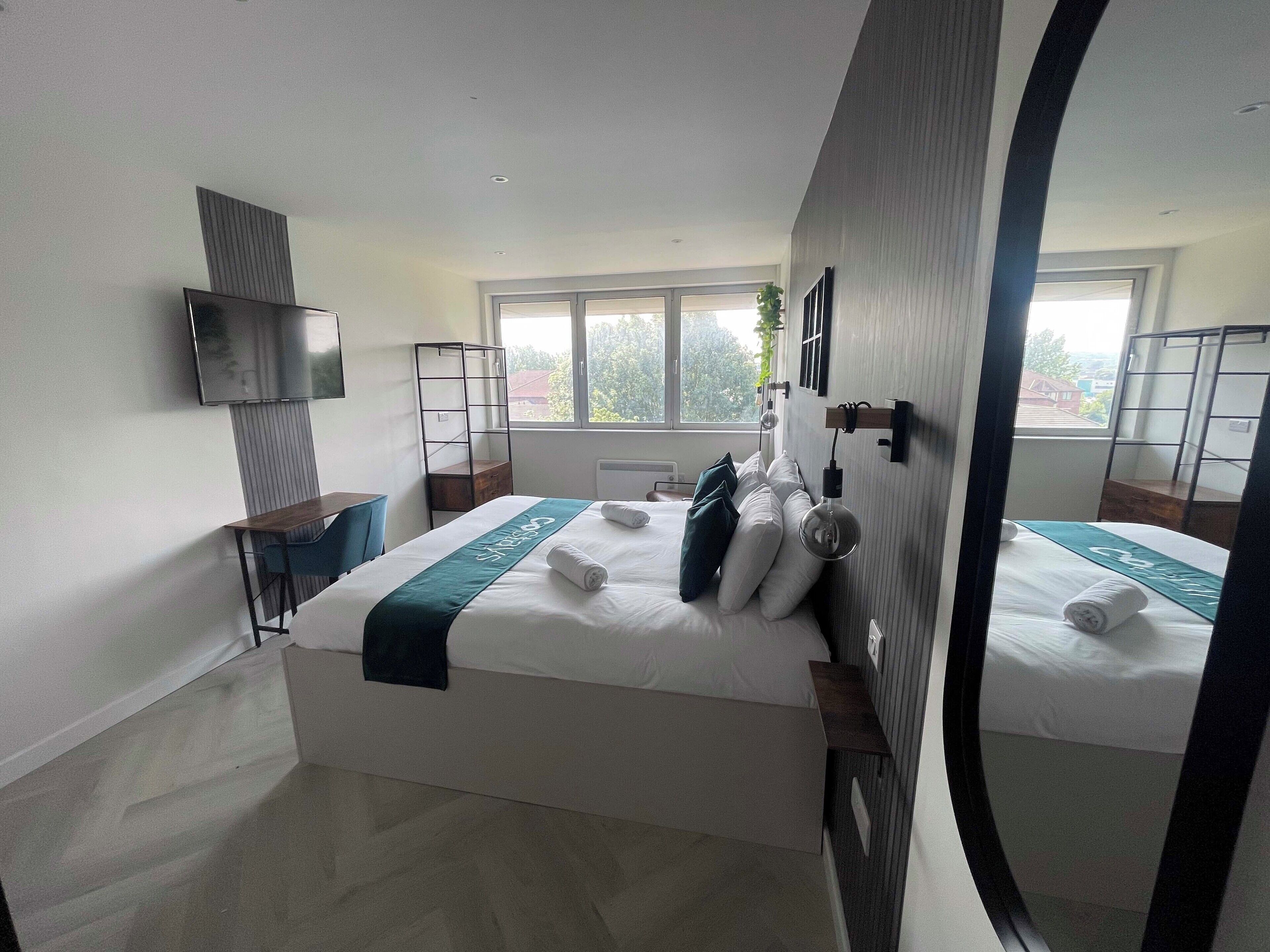 A hotel room with a bed, a desk, a TV, and a window.