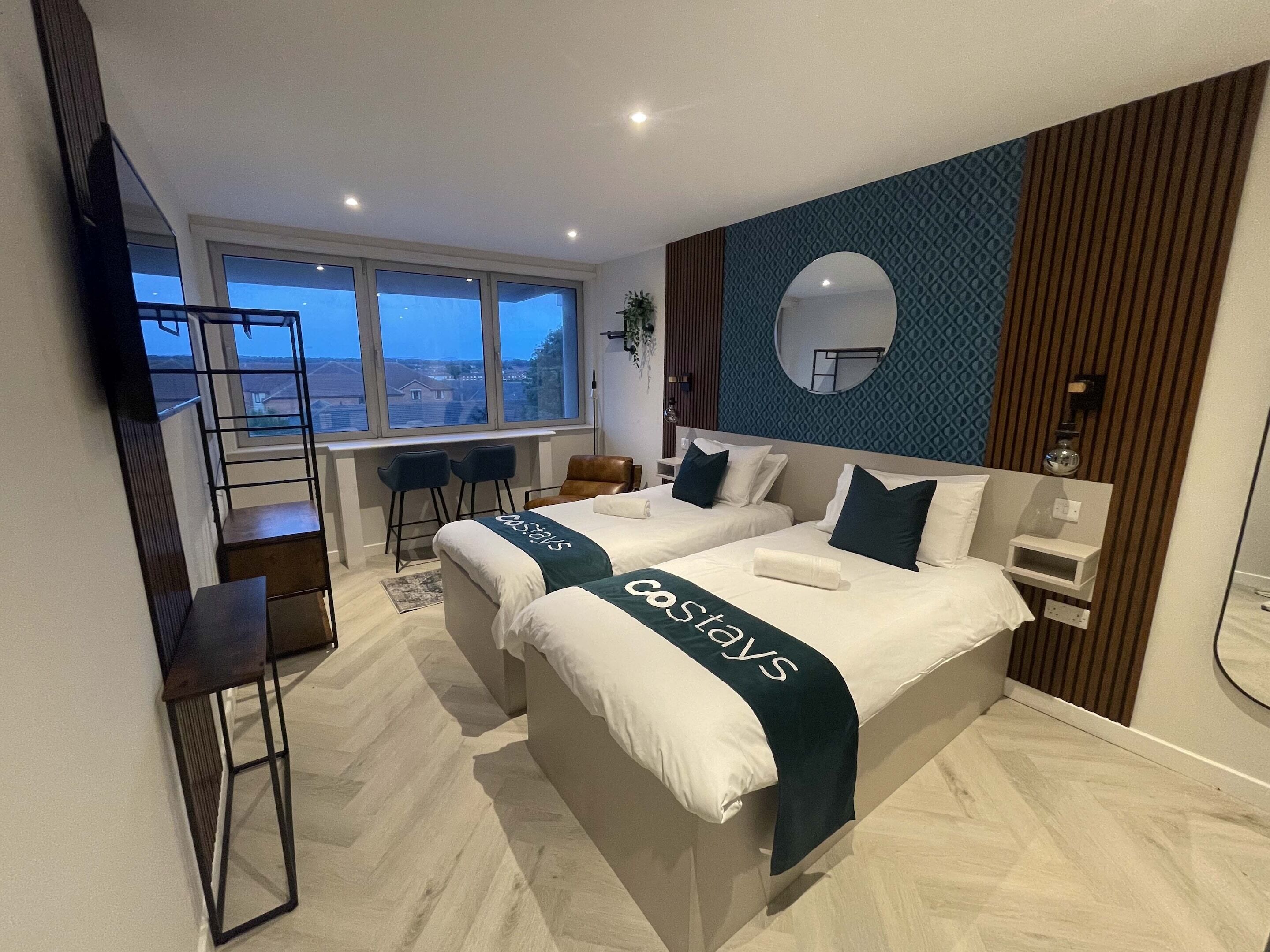 Una habitación de hotel moderna con dos camas, un ventanal grande, un televisor y un balcón.