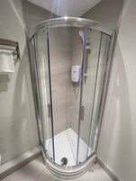 A glass-enclosed shower stall with a white handheld showerhead and a soap dispenser on the wall.