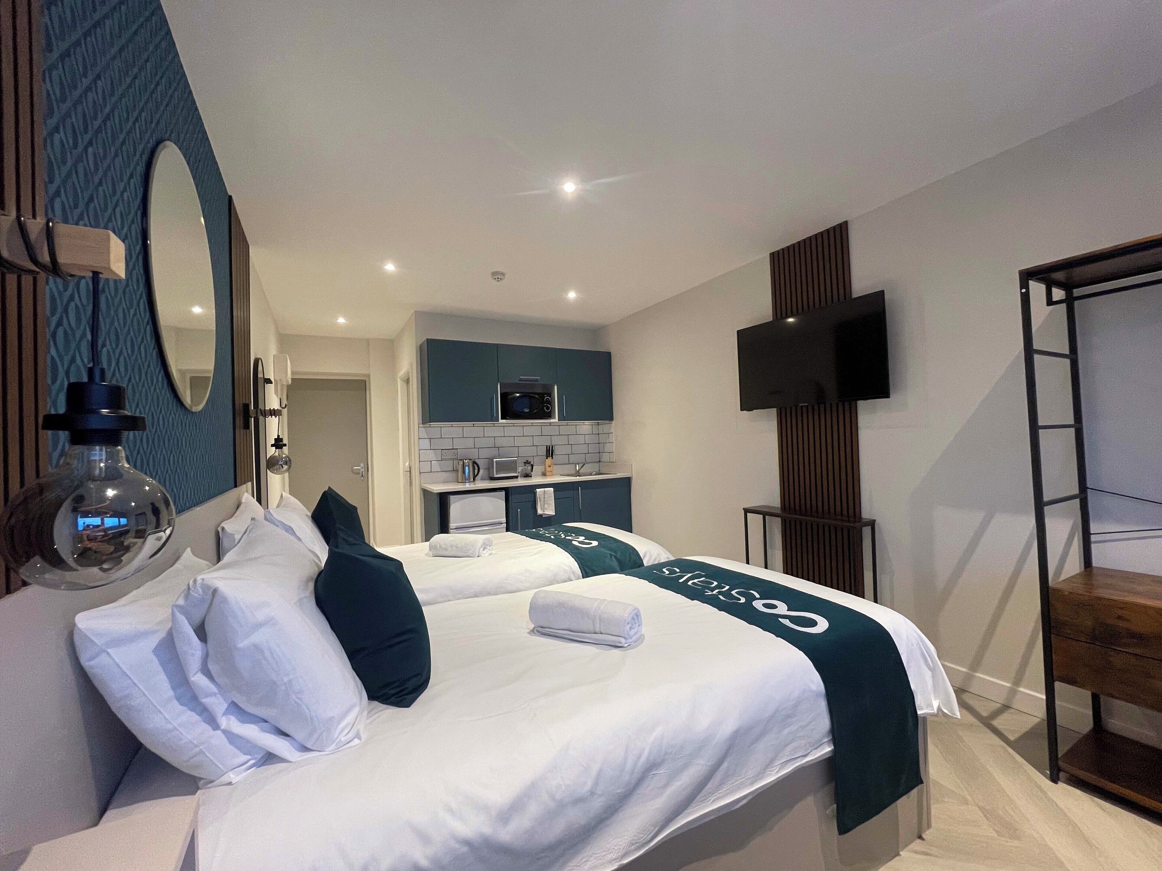 Une chambre d’hôtel avec un grand lit, une petite kitchenette, une télévision et une échelle.