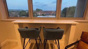 A room with a large window overlooking a residential area, a built-in desk, and two chairs.