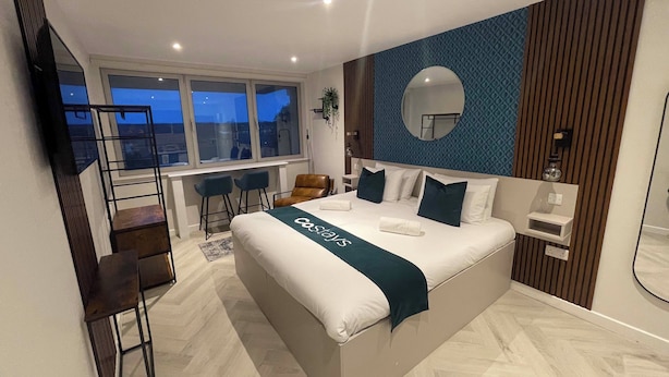 A modern hotel room with a large bed, a balcony, and a view of the city at dusk.