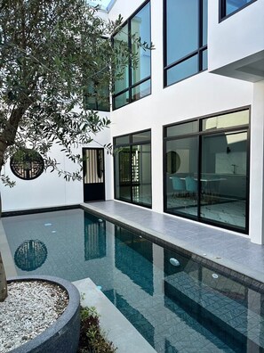 Un bâtiment moderne doté d’une piscine, de grandes fenêtres et d’un arbre.
