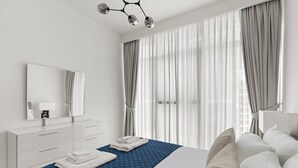 Une chambre à coucher moderne avec un grand lit, une table de chevet, un miroir et une fenêtre avec des rideaux.