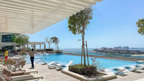 Un espace aménagé au bord de la piscine, avec des chaises longues, une vue dégagée sur la mer et un bâtiment moderne en arrière-plan.